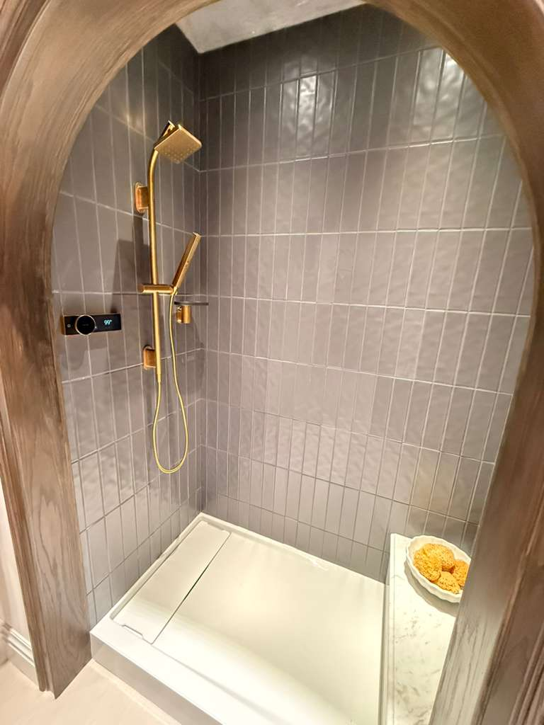 Shower with unique arched niche, slate-blue vertical tile, and gold fixtures in Bradenton home