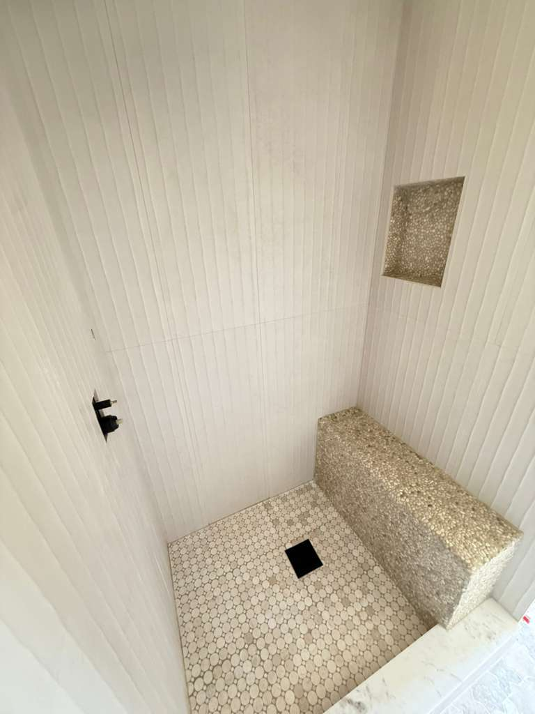 Custom shower with ribbed white tile walls and pebble mosaic bench — Schluter waterproofed installation in Siesta Key