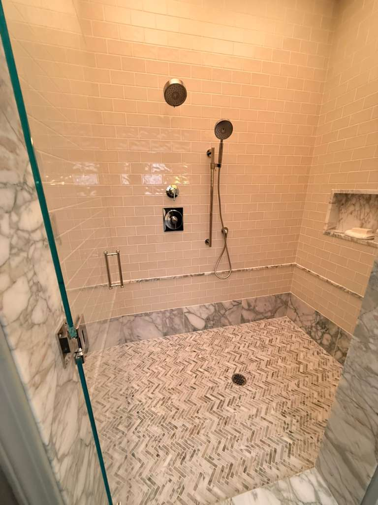 Shower with cream subway tile walls and herringbone marble mosaic floor — Schluter waterproofing system installed in Sarasota